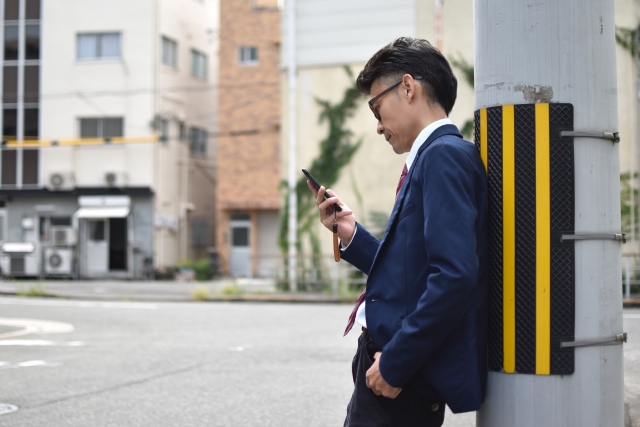 電柱にもたれてスマホを見る男性